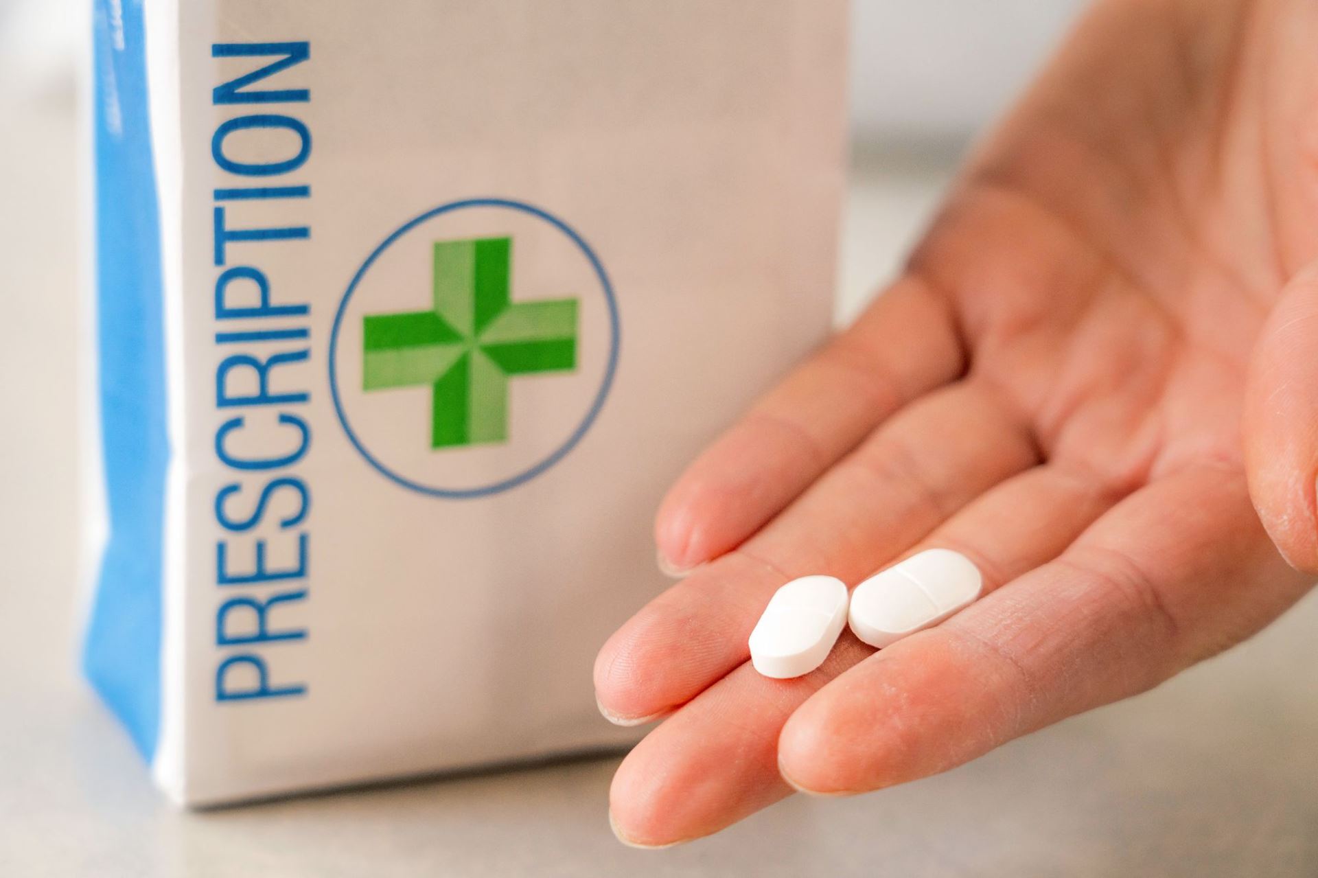 Paper bag from Pharmacy with hand holding two tablets picture linked to repeat prescription information